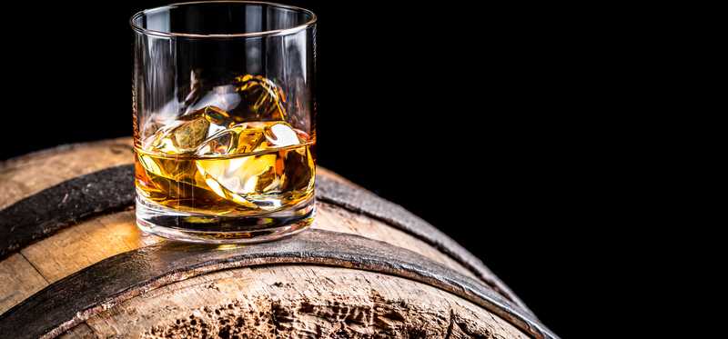 Glass of whiskey sitting on a barrel.
