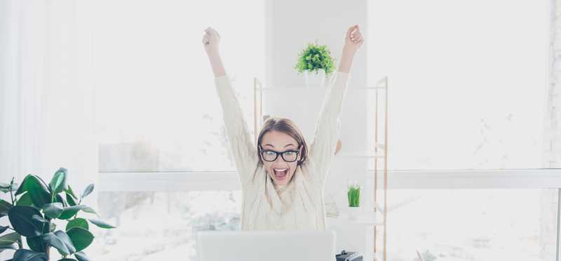 A woman celebrating with hands in the air from her desk