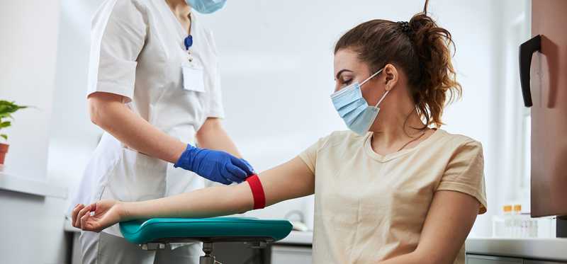 Person wearing mask and sitting in wheelchair receives medical treatment in hospital.