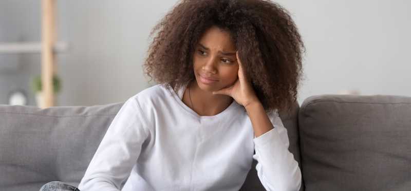 Person sits on couch frowning while holding smartphone.