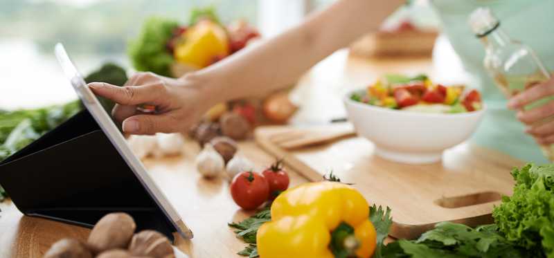 Woman checking tablet with vegetables on the counter.