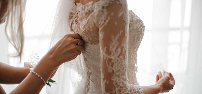 Woman helping bride put on bridal gown