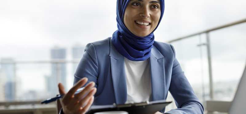 Person in business suit in front of computer while speaking.