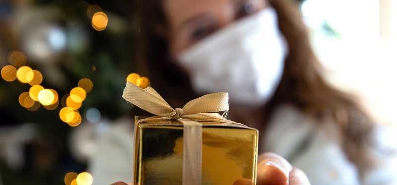 Woman in mask holding out gold wrapped gift box