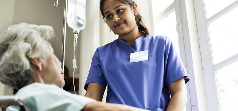 Woman in scrubs standing in front of elderly patient.