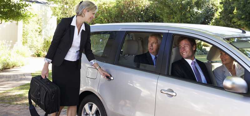 Woman in a suit getting into a car with other professionals.