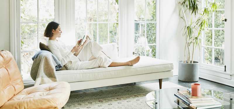 Person sitting on a white couch in a sunroom with large windows