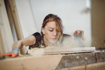 Light haired woman wearing protective glasses while woodworking