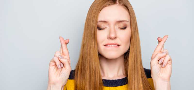 Woman with eyes closed and fingers crossed.