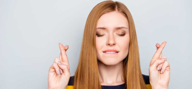 Person with eyes closed and fingers crossed.