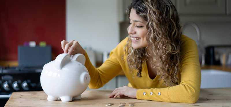Woman with long curly hair puts coins in piggy bank