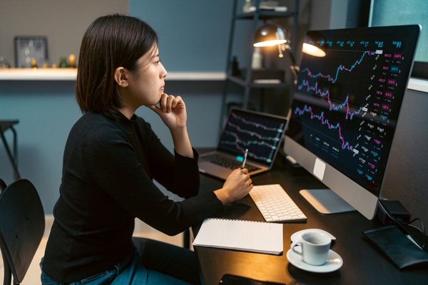 A woman sitting at her desk looking at stock charts on her computer.