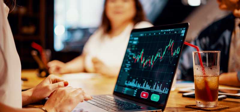 Woman sitting at table with others and looking at stock chart on laptop