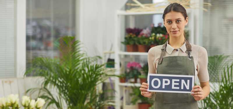 Worker in floral shop holding open sign.