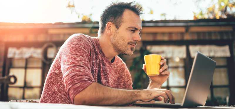 Person holding cup while using laptop.