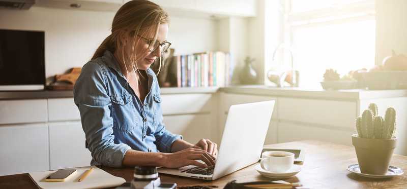 Person typing on laptop on kitchen counter.