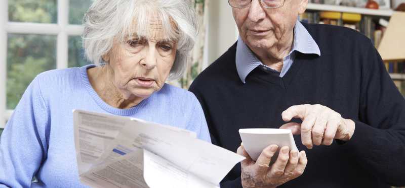 Worried senior couple using calculator and looking at bill