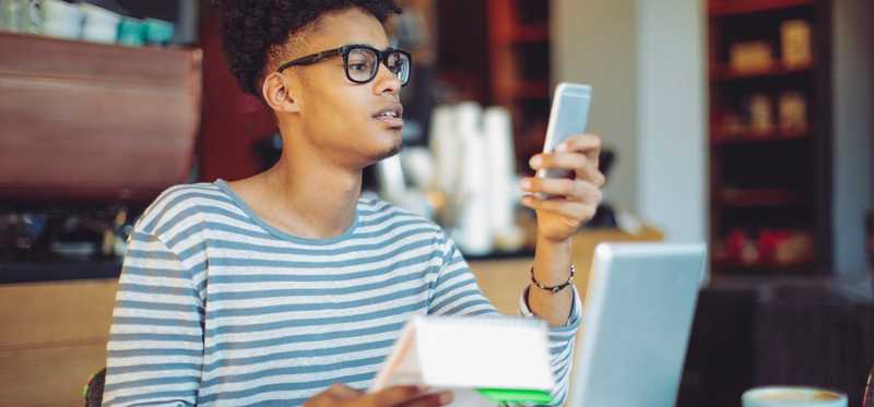 Person looks at phone and paperwork at desk.