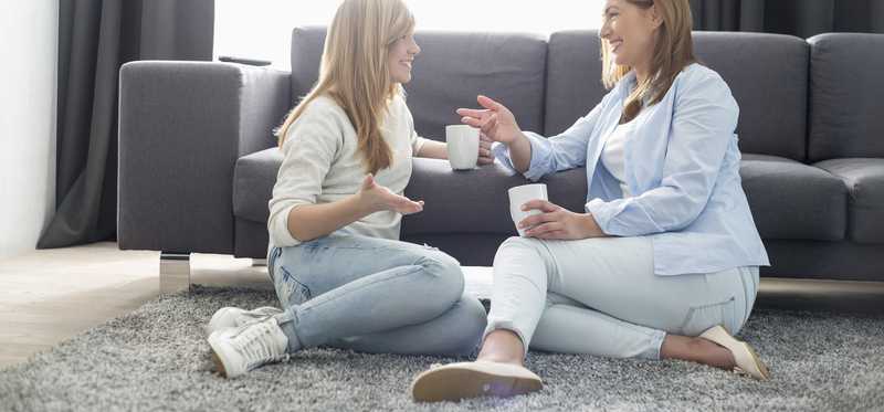 Young female adult and older female adult talk while sitting on a rug.