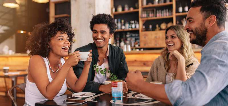 Friends laughing and enjoying a cup of coffee at a coffeeshop.