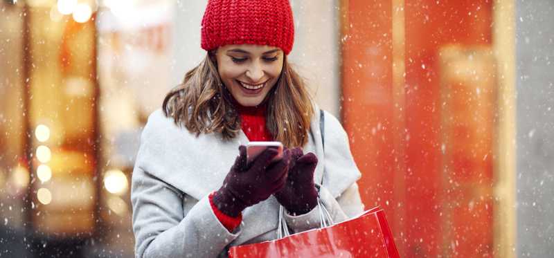 Young woman in winter shopping and smiling while looking at phone