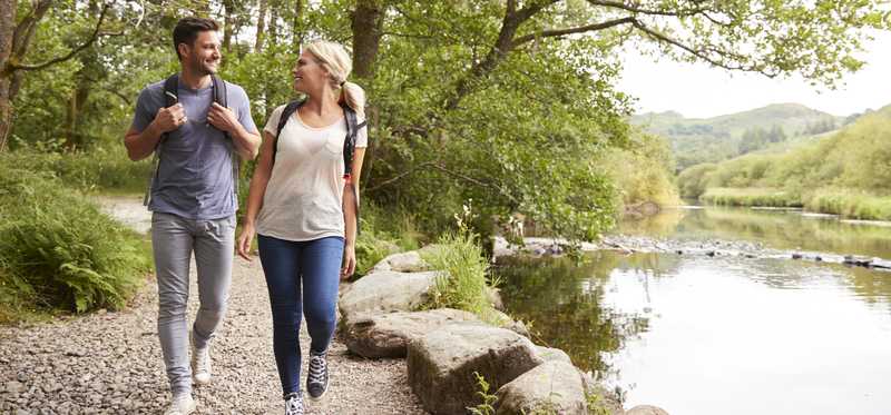 Two people walk outside on trail near lake.