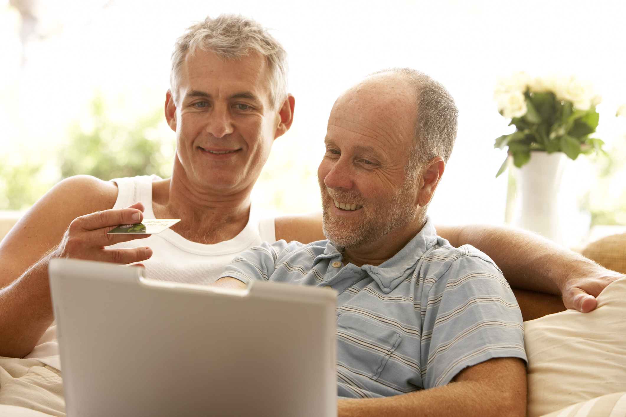 Two adults smile as one holds credit card and the other holds laptop.