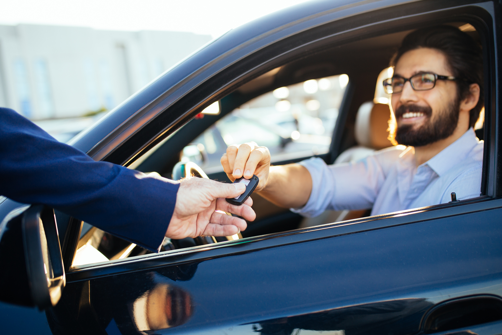 Person hands car keys to person sitting inside a car. A person hands car keys to someone sitting inside a car.