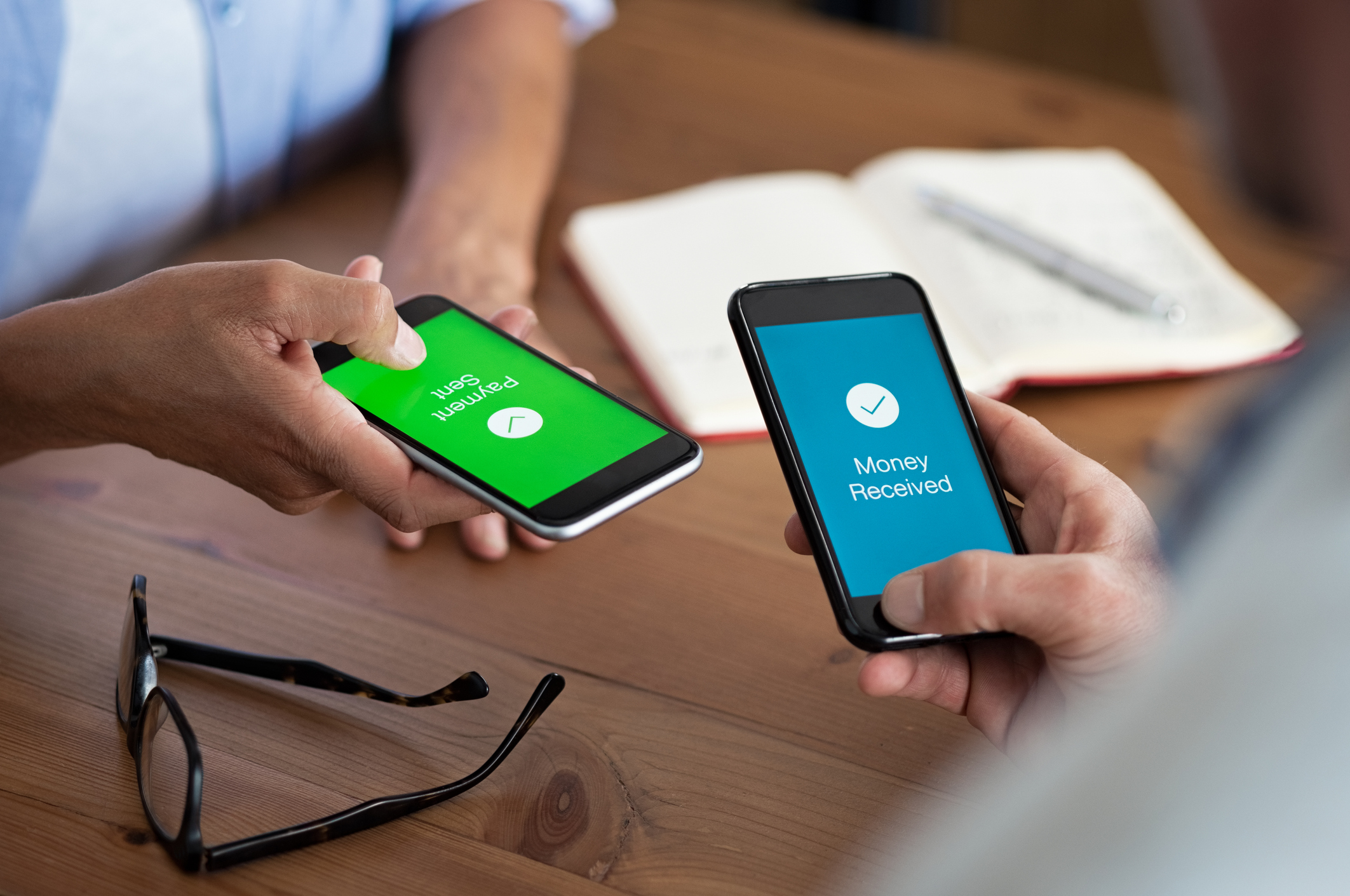 two people holding cell phones that show money being transferred between the two people Two people holding cell phones that show money being transferred between them