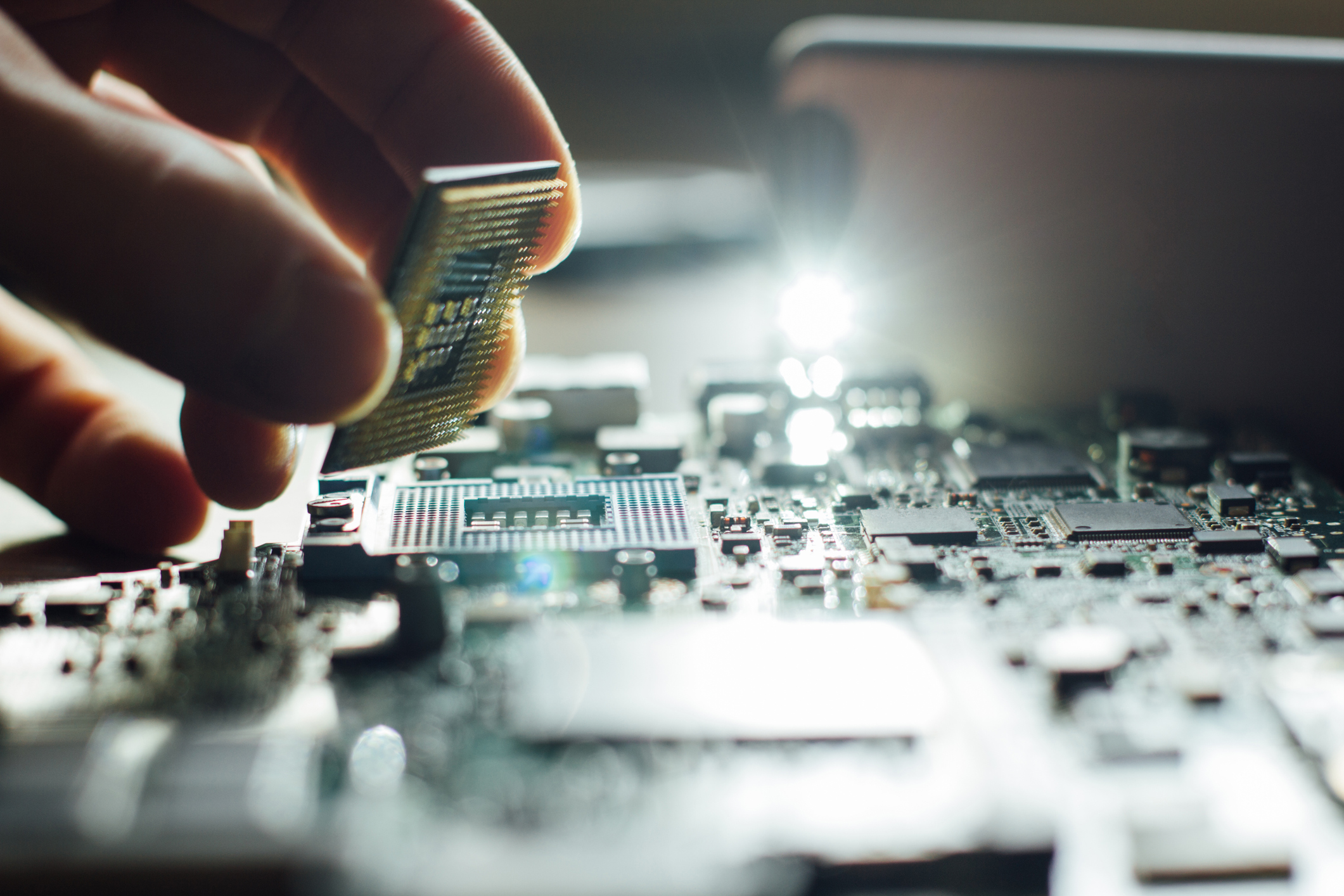 A hand holding a microchip above a circuit board A hand holding a microchip above a circuit board.