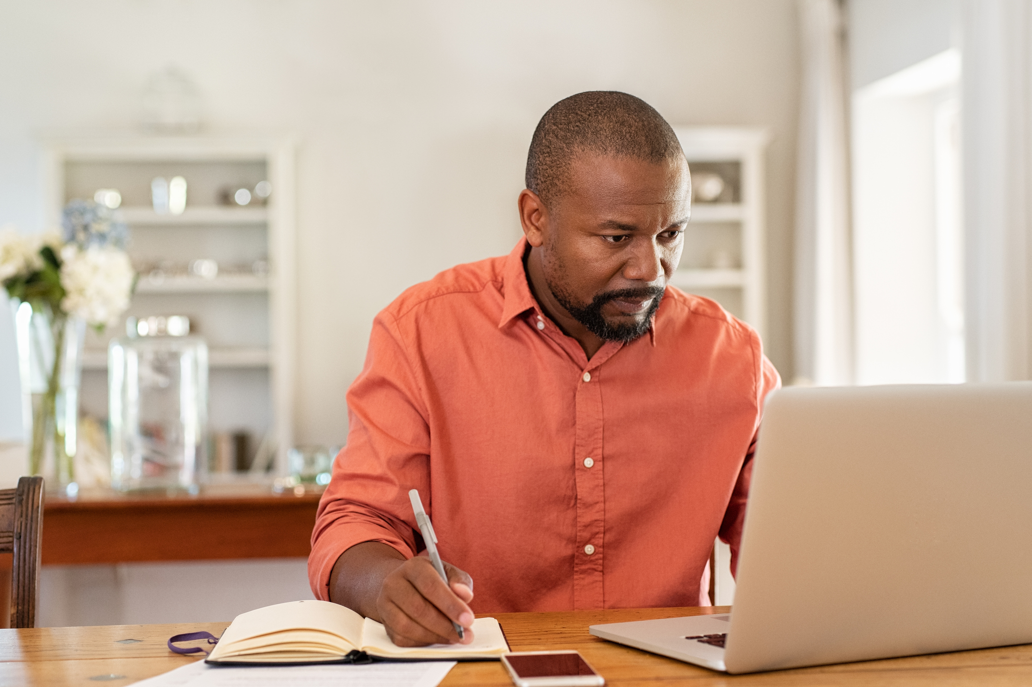 Person looking at computer and writing in book. Person doing research at a computer and writing in a book.