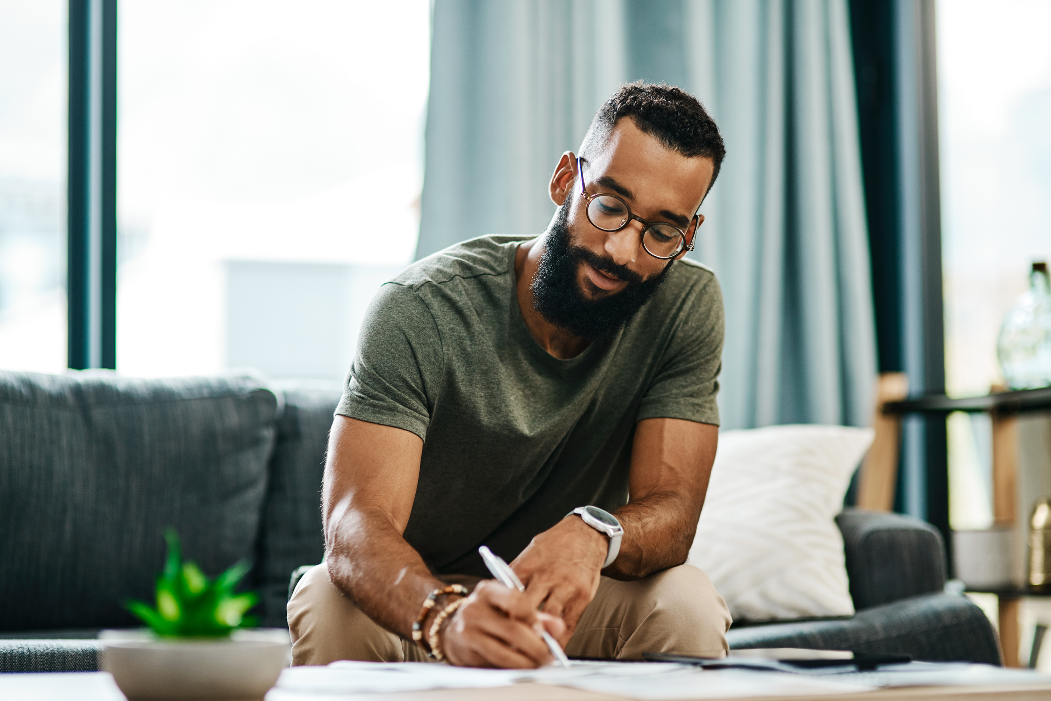 Man sitting on couch is writing on paperwork on coffee table. Person sitting on couch and writing on paperwork on coffee table.