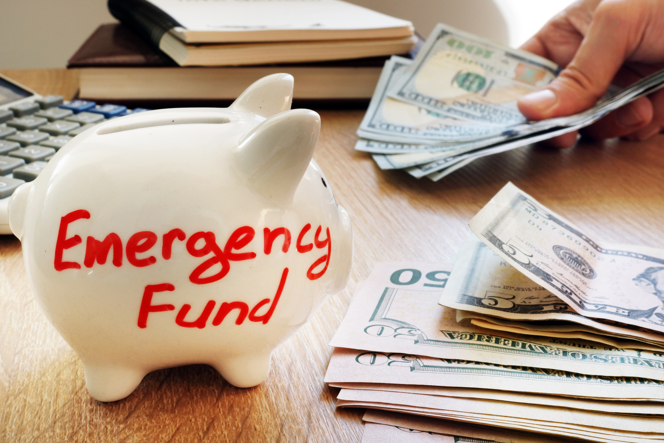 Piggy bank labeled Emergency Fund Piles of cash lying around a piggy bank labeled Emergency Fund.