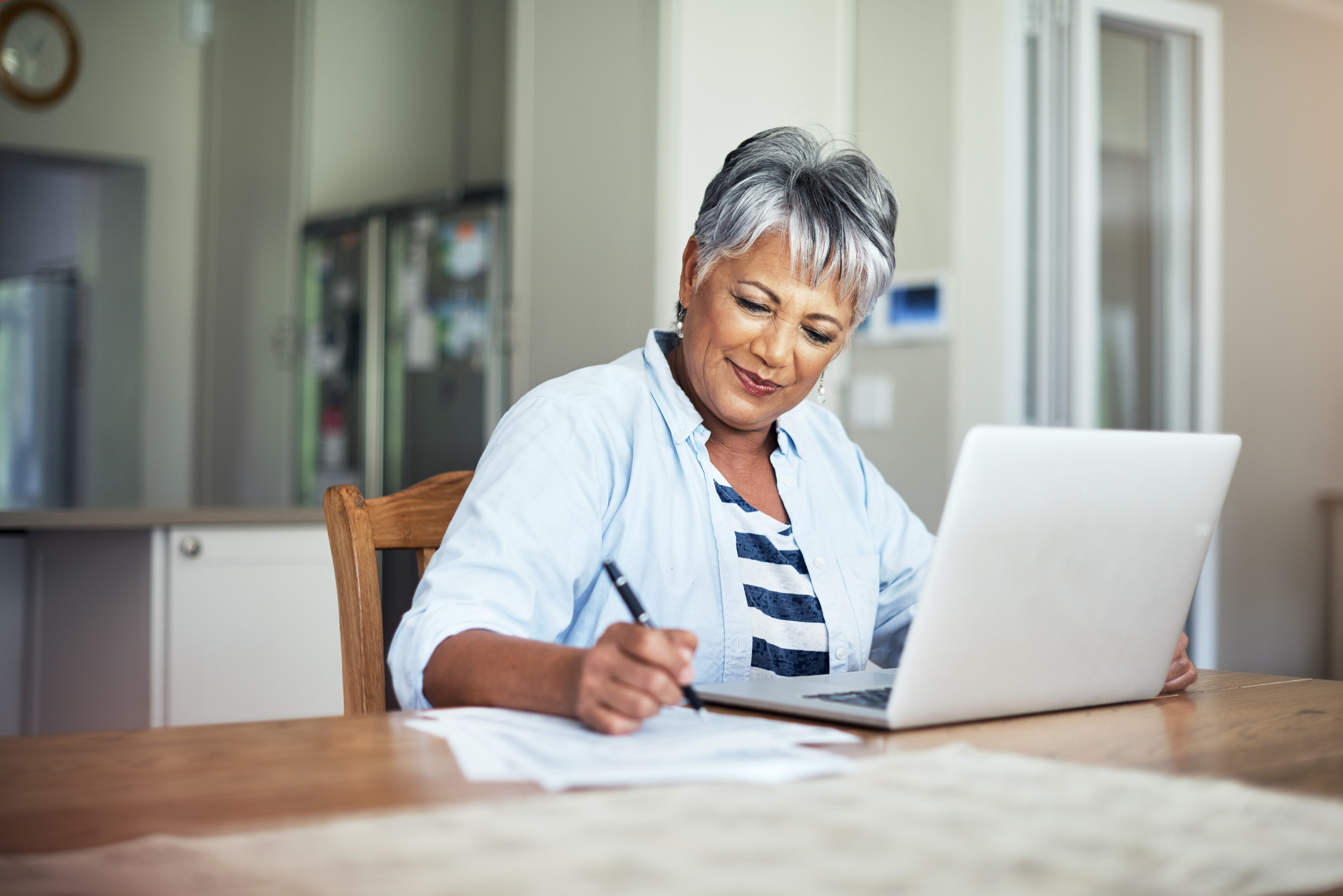 4-senior-budgeting.jpg Smiling person takes notes in front of laptop at home.
