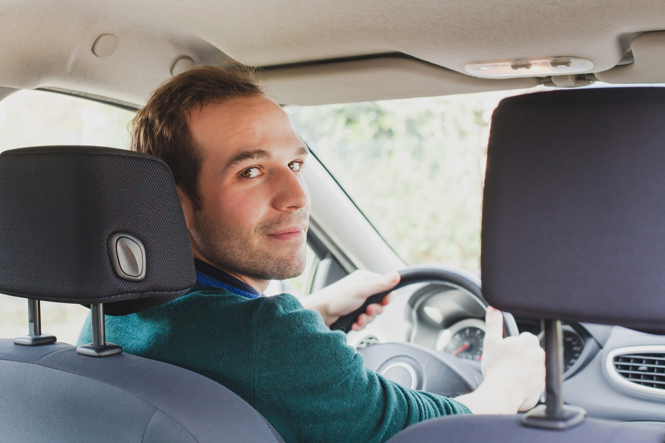 A side gig - driving We see a young man in a car's driver's seat, turning around to look at someone in the back seat.