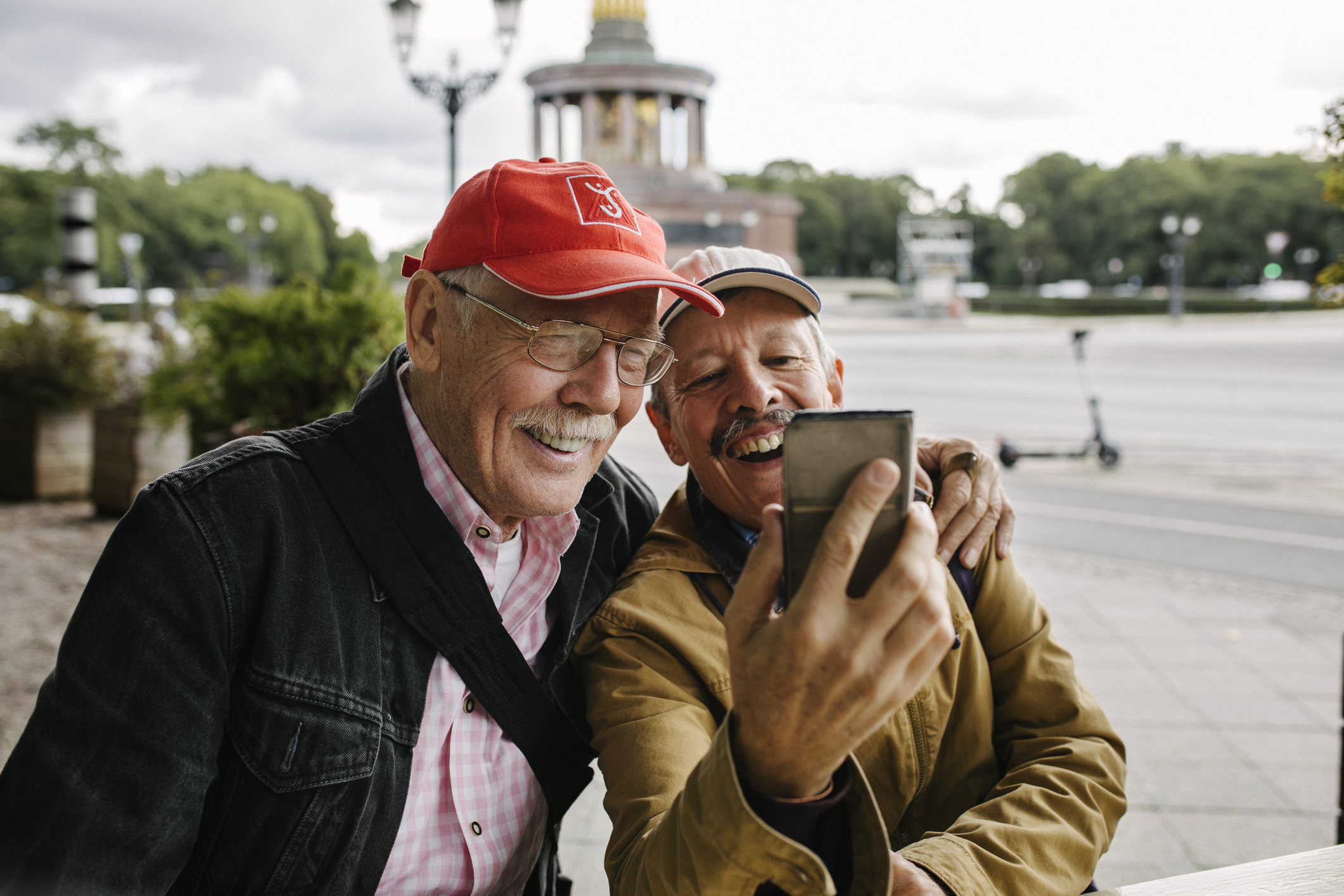 Two happy seniors look at phone while outdoors.