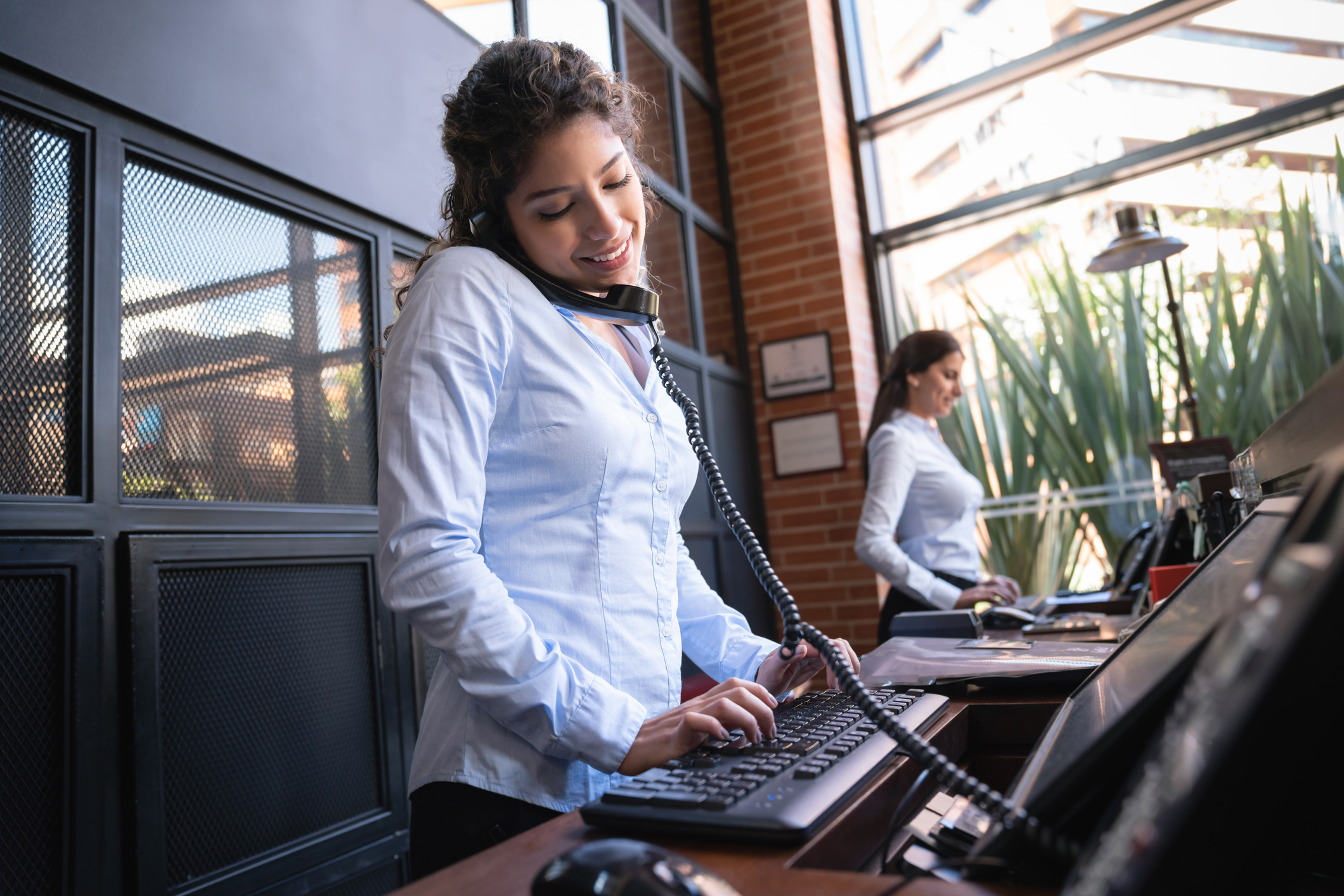A receptionist answering the phone and typing on a computer at a hotel front desk.