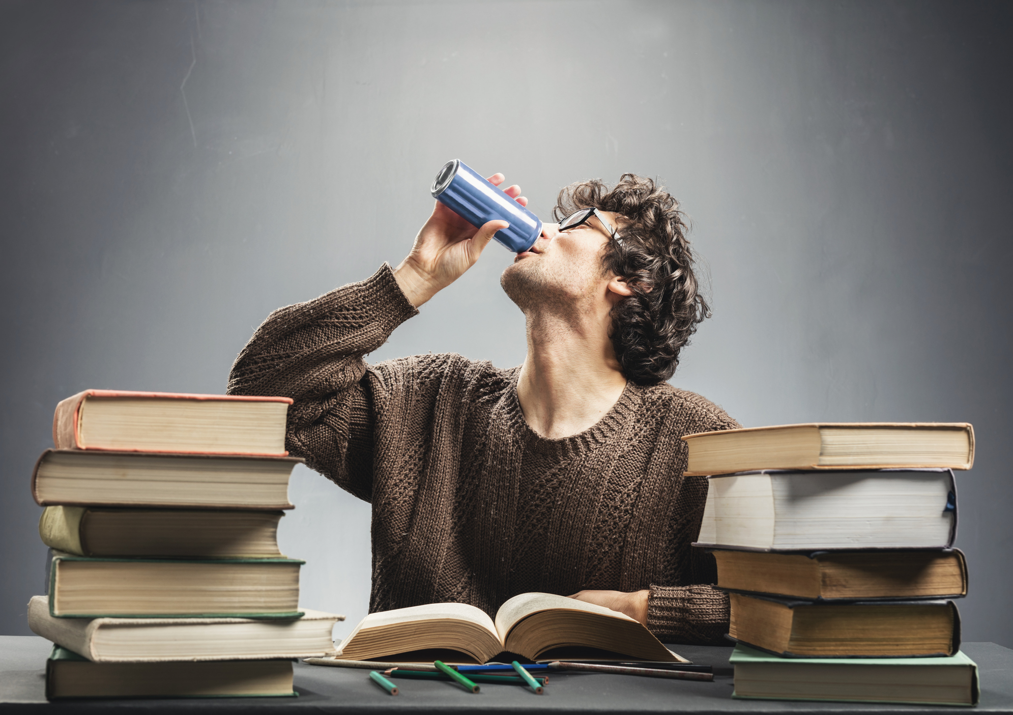 Person drinking from a can in the middle of stacks of books Person drinking from a can in the middle of stacks of books