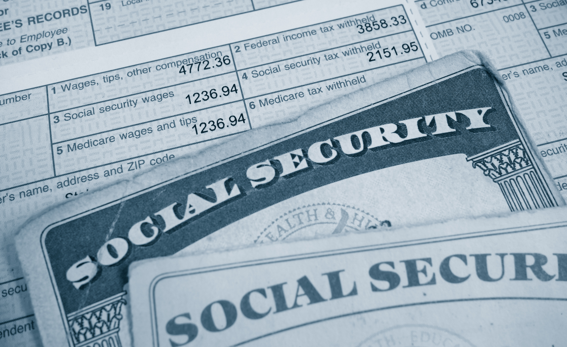 A Social Security card lying atop a W2 tax form, highlighting payroll taxes paid. A Social Security card lying atop a W2 tax form, highlighting payroll taxes paid.
