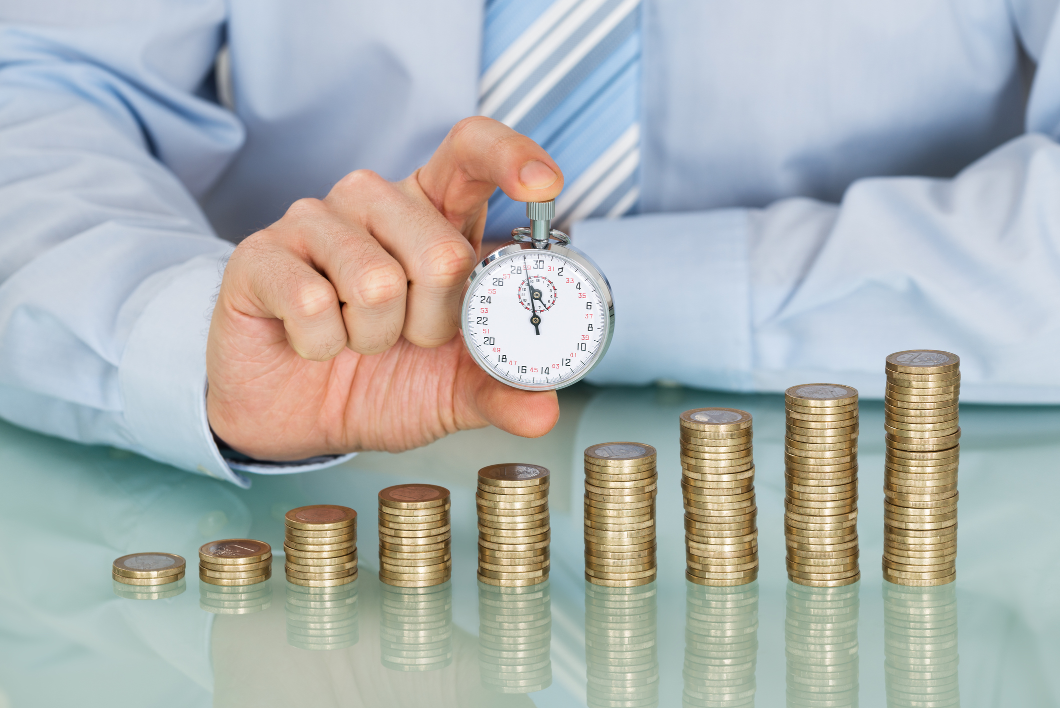 growing your money, coins, dividends, time A businessperson holding a stopwatch behind ascending stacks of coins.