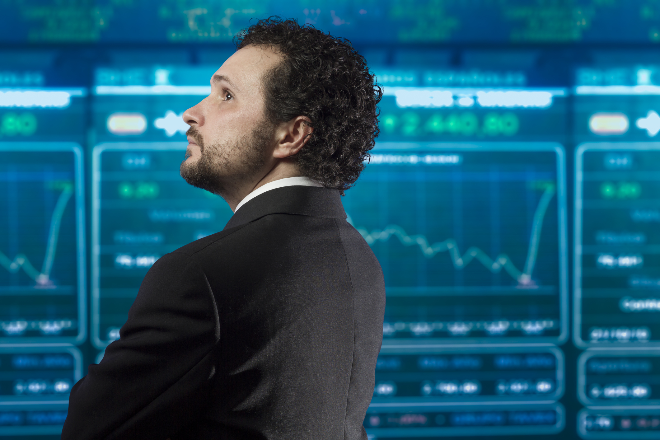 A businessman looking at a digital board containing stock quotes.