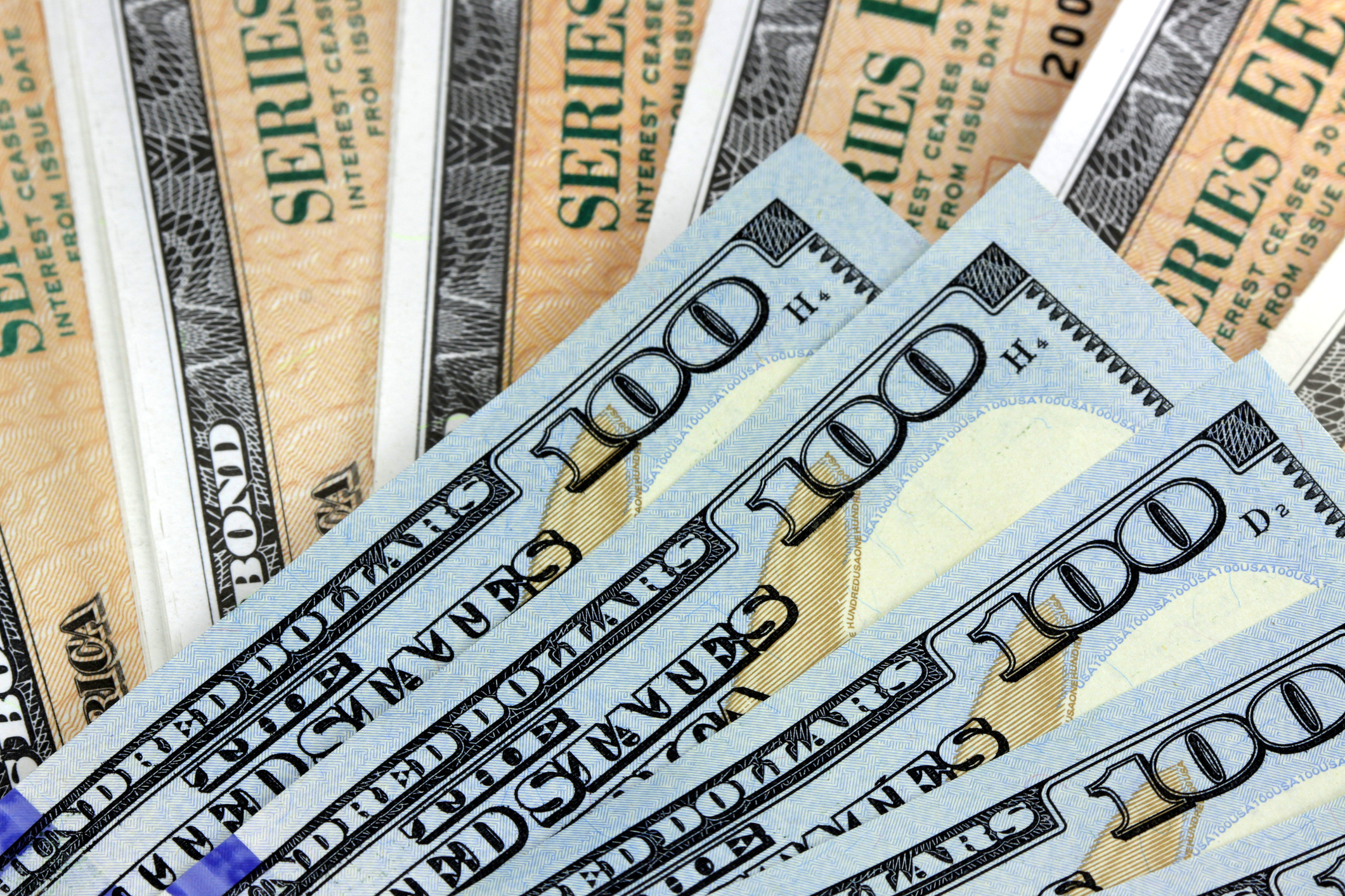 A fanned pile of hundred dollar bills lying atop Treasury bonds