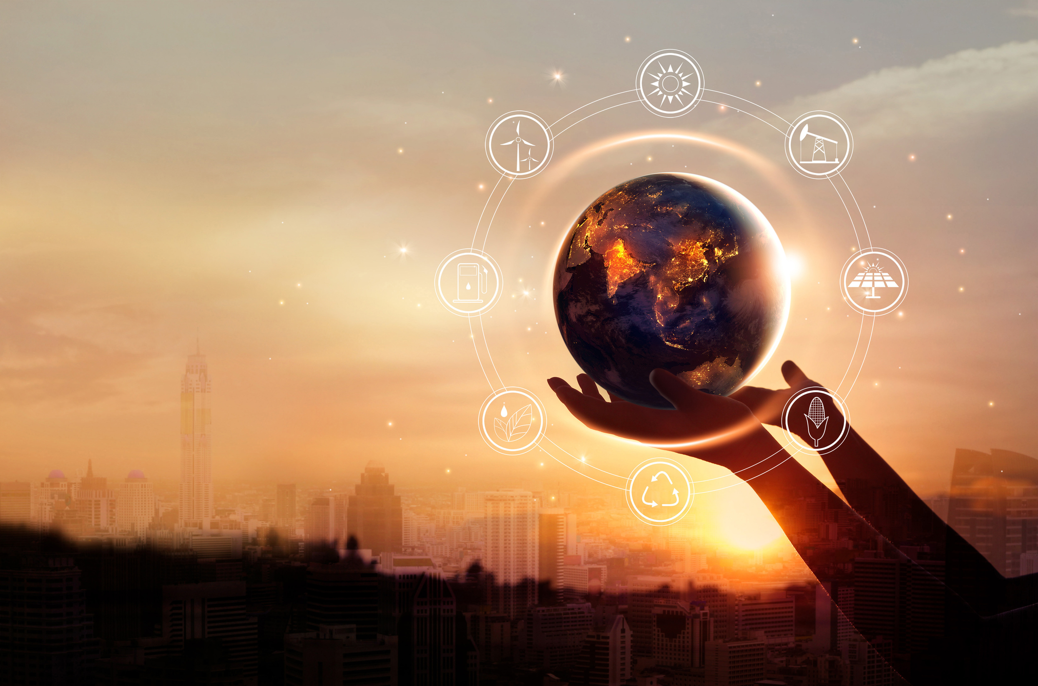 A person holding a globe with renewable energy images around it an a cityscape in the background. A person holding a globe with renewable energy images surrounding it and a cityscape in the background.