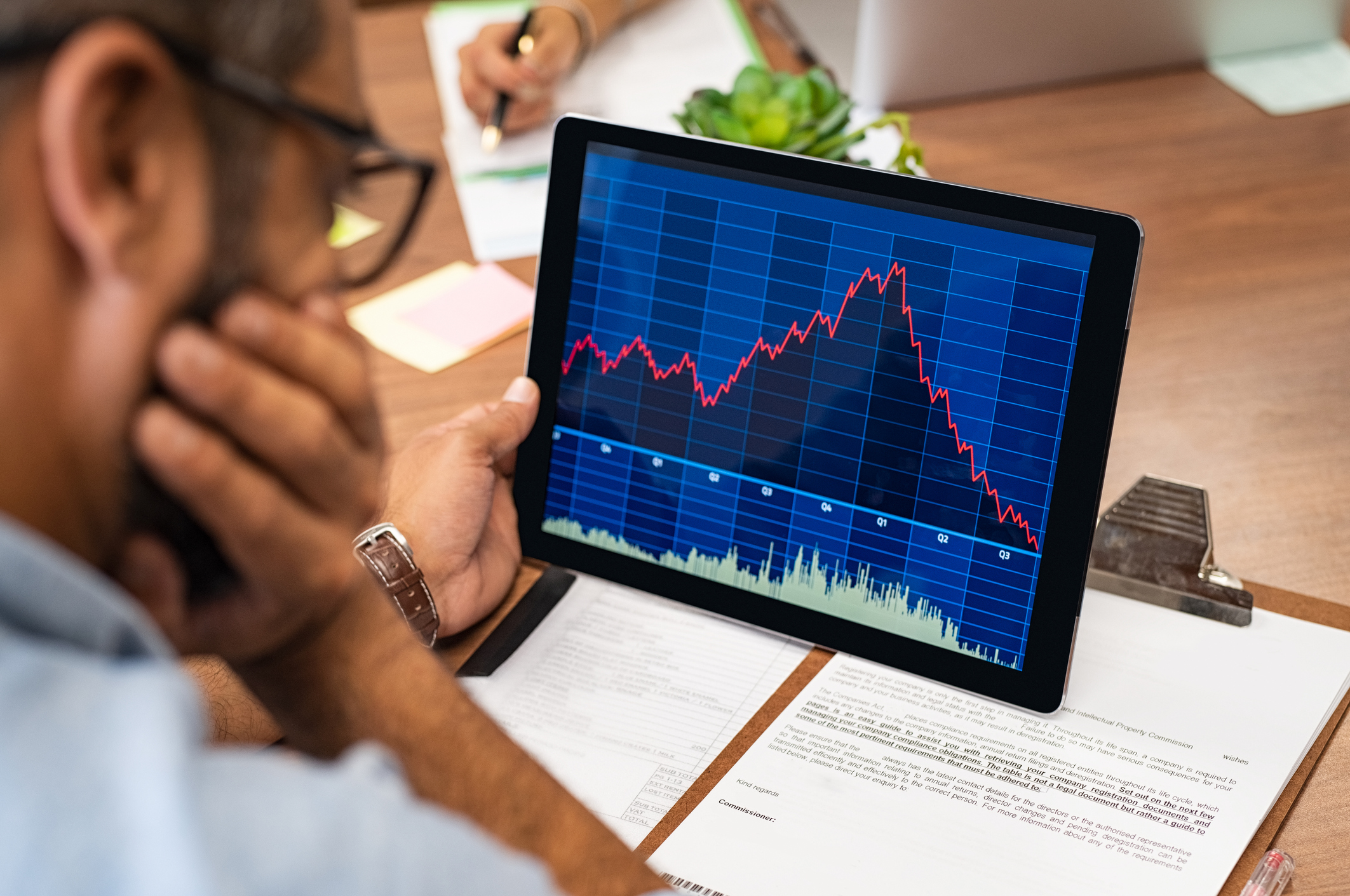 A person looking at a red stock chart on a tablet. A person looking at a red stock chart on a tablet.