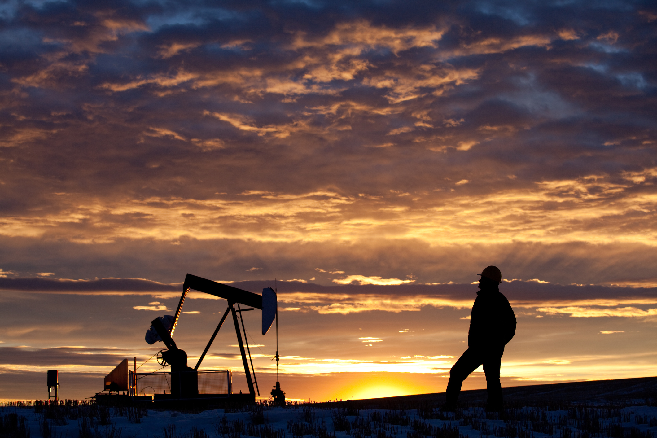 A person looking at an oil pump with the sun setting in the background. A person looking at an oil pump with the sun setting in the background.