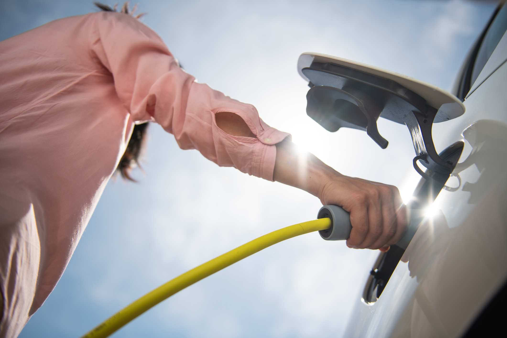 A person plugging in an EV to recharge the battery. A person plugging in an EV to recharge the battery.