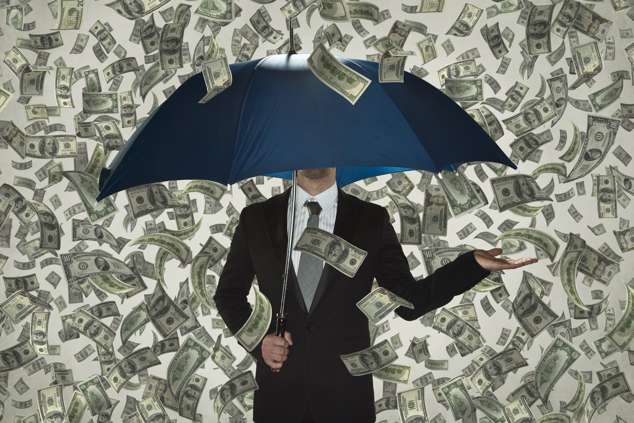 Businessman holding umbrella as money rains down