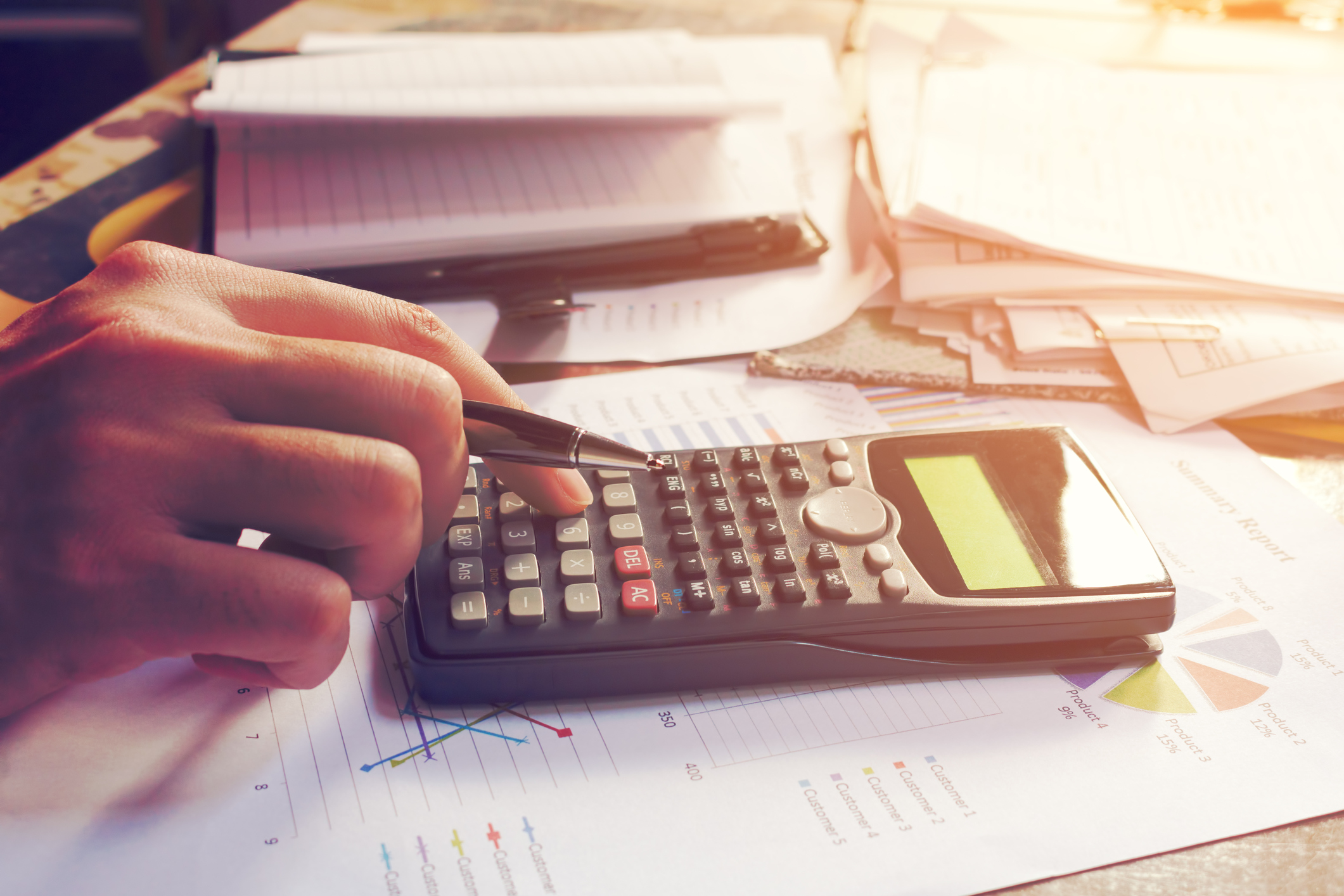 Calculator and paperwork on desk A hand using a calculator on a desk filled with paperwork.