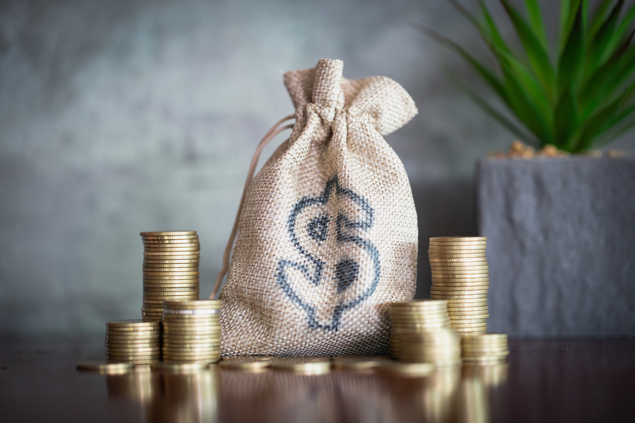 Stack of gold coins next to burlap bag with dollar sign Stacks of coins next to a burlap bag with dollar sign.