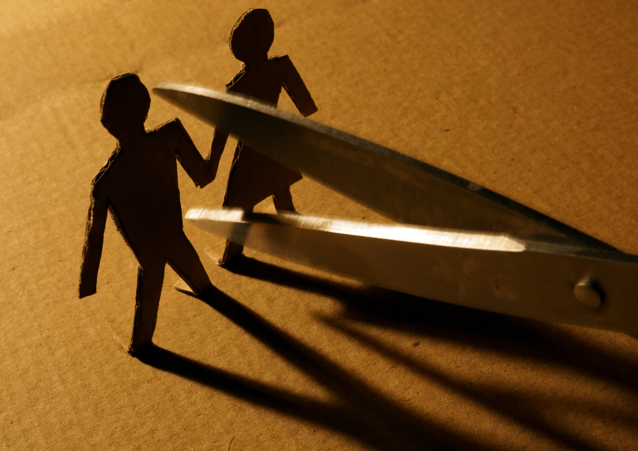 Paper people holding hands about to be separated with scissors. Paper people holding hands about to be separated with scissors.